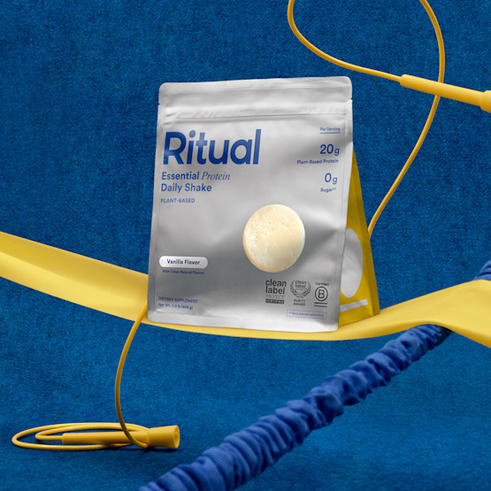 A bag of Essential Protein Daily Shake with blue background and yellow exercise equipment props.