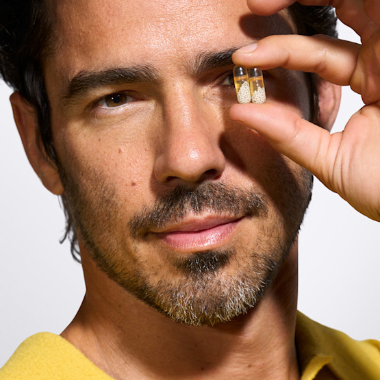 Male model holding two capsules in hand in front of left eye.
