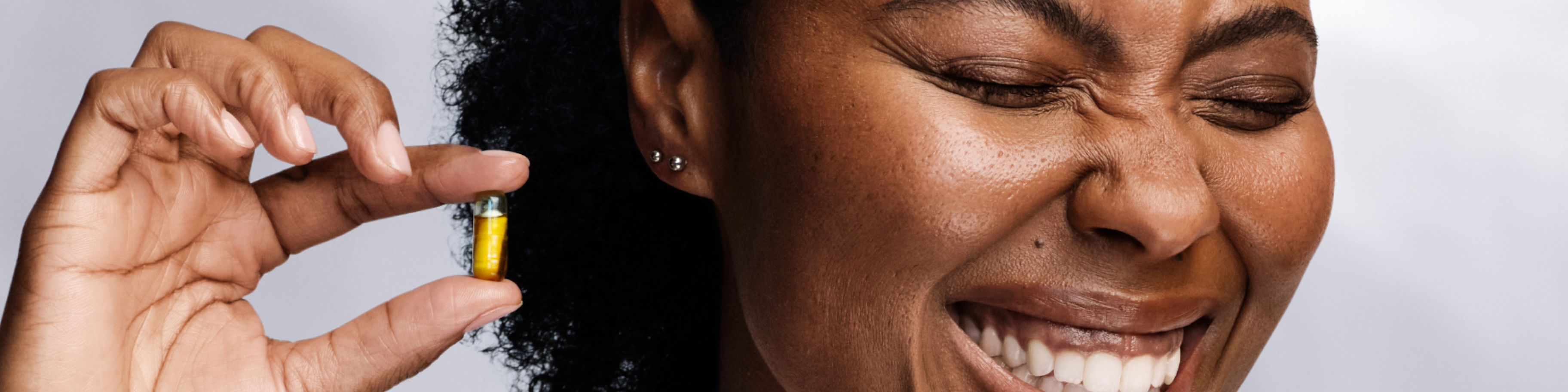 Woman holding a HyaCera capsule while smiling and scrunching her nose.